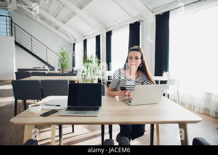 Jeune femme sérieuse d'affaires est assis dans un café avec ordinateur portable et téléphone portable et à la recherche à l'appareil photo. Banque D'Images