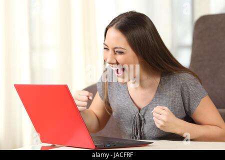 Bonne nouvelle lecture femme excité à la ligne dans un ordinateur portable rouge dans une house interior Banque D'Images