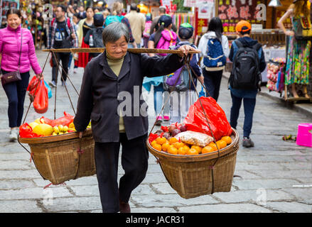 Yangshuo, Chine. Femme portant de lourdes Panier de fruits sur l'épaule du pôle. Banque D'Images