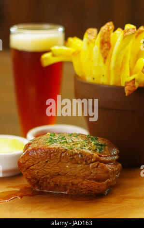 Close up d'un bien-fait le boeuf mariné grillé bifteck avec du ketchup, de la moutarde et de frites avec un verre de bière derrière sur planche de bois Banque D'Images