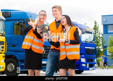 Logistique - fier conducteur ou le transitaire et collègues avec ordinateur tablette, en face de camions et remorques, sur un point de transbordement, un bon son et une équipe performante Banque D'Images