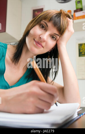 Kopf-und-Schulter-Ansicht eines jungen Frau am Tisch, brünetten Schreibstift sitzend mit der und Schnellhefter en main vor sich liegend Banque D'Images