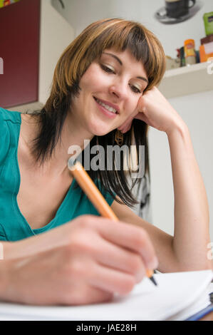 Kopf-und-Schulter-Ansicht eines jungen Frau am Tisch, brünetten Schreibstift sitzend mit der und Schnellhefter en main vor sich liegend Banque D'Images