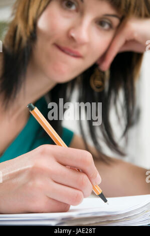 Kopf-und-Schulter-Ansicht eines jungen Frau am Tisch, brünetten Schreibstift sitzend mit der und Schnellhefter en main vor sich liegend Banque D'Images