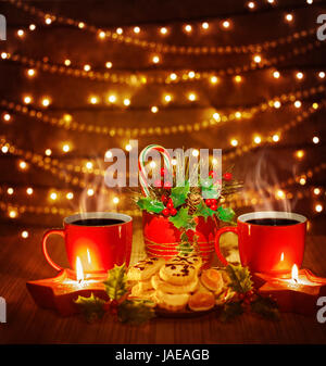 Belle photo de Noël encore la vie, thé rouge tasses avec de délicieux biscuits maison et des bougies sur la table en bois sur fond marron brillant, Garland électrique sur le mur rougeoyant, Candy Cane Banque D'Images