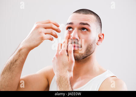 Jeune homme est l'application de gouttes pour les yeux. Banque D'Images