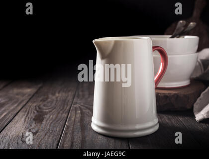 Pichet blanc céramique avec poignée rouge sur la table en bois sombre. Pitcher. Banque D'Images