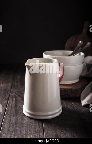 Pichet blanc céramique avec poignée rouge sur la table en bois sombre. Pitcher. Banque D'Images