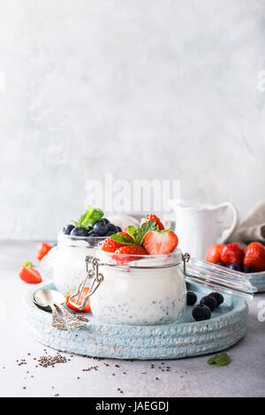 Chia Pudding pour le petit-déjeuner dans des bocaux en verre garni de Berry en deux parties sur fond noir en gris clair avec une serviette et de cuillères. Copier l'espace. Banque D'Images