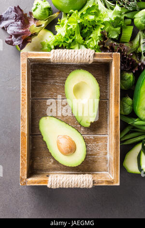 Avocat en plateau en bois avec un assortiment de légumes verts, salade, poivrons et choux de Bruxelles sur la table en pierre marron clair. Concept d'aliments sains wi Banque D'Images