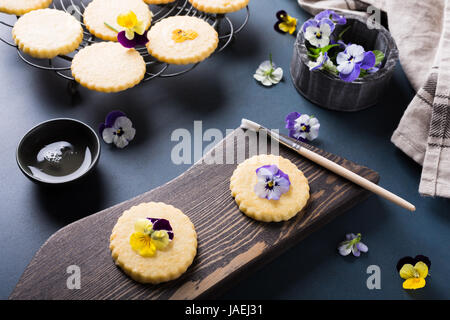 Processus de fabrication de biscuit avec des fleurs comestibles sur le vieux fond de bois. Maison de l'alimentation Banque D'Images