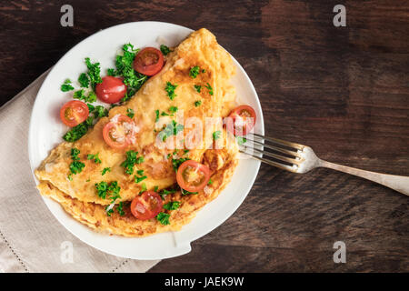 Une photo d'une omelette aux tomates cerises, le persil et le fromage râpé, tourné à partir de ci-dessus sur une texture rustique en bois avec une place pour le texte Banque D'Images