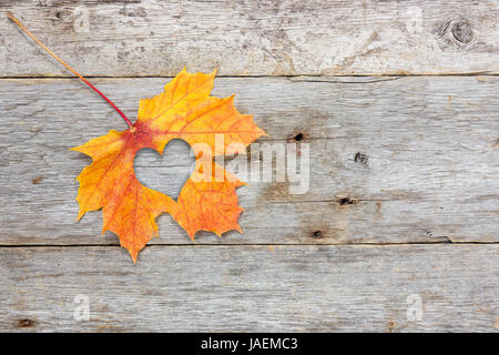 Tomber en amour photo métaphore. Feuille d'érable avec forme de coeur sur le fond en bois Banque D'Images