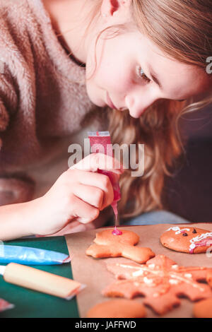 Girl decorating Christmas gingerbread cookies au four avec un stylo au chocolat Banque D'Images