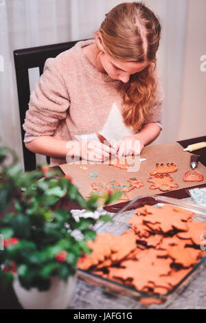 Girl decorating Christmas gingerbread cookies au four avec un stylo au chocolat Banque D'Images