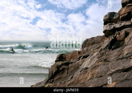 Nettoyer magnifique océan atlantique des surfeurs attraper les vagues avec des rochers en premier plan sur la côte d'Irlande Banque D'Images