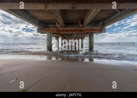 La vue de dessous un pier/jetty sur une plage avec des vagues clapotis calmement contre la plage de sable Banque D'Images