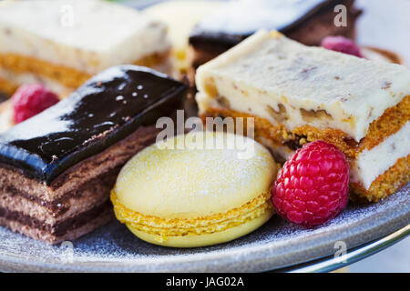 Gros plan d'une sélection de gâteaux, une tranche de crème et d'un macaron et une framboise sur une assiette, le thé de l'après-midi. Banque D'Images
