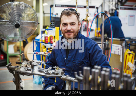 Un homme, un employé d'usine assis à un établi, à côté d'un grand fan de metal. Banque D'Images