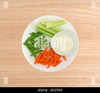 Vue de dessus du céleri, carottes et pois mange-tout sur une assiette avec un bol de sauce ranch sur le côté sur une table en bois. Banque D'Images