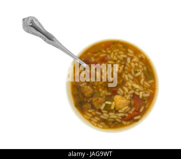 Vue de dessus d'un bol de gumbo avec viandes, le riz et les légumes dans un bouillon avec une cuillère dans l'aliment isolé sur un fond blanc. Banque D'Images