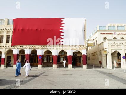 Deux hommes en robes traditionnelles Qatari autour de le souk sous un drapeau géant du Qatar dans le centre de Doha Banque D'Images