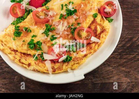 Une photo gros plan d'une omelette aux tomates cerises, le persil et le fromage râpé, tourné à partir de ci-dessus sur une texture rustique en bois avec une place pour le texte Banque D'Images
