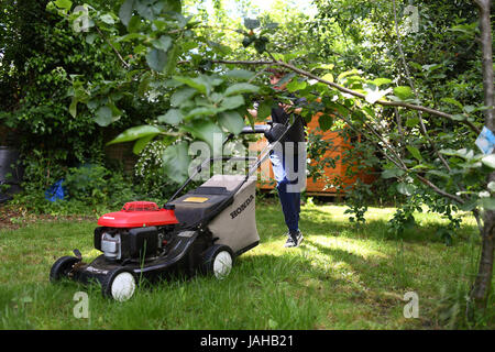 Un jeune garçon coupe l'herbe dans le jardin dans le cadre de ses tâches pour obtenir de l'argent de poche Banque D'Images