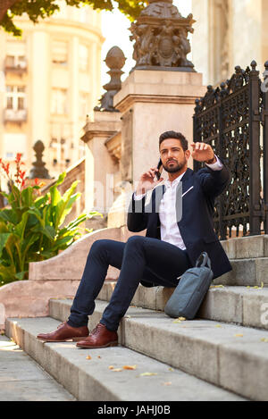 Un beau jeune homme assis sur l'escalier en conversation sur son smartphone et en agitant à quelqu'un à la basilique à Budapest en Hongrie. Banque D'Images