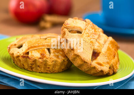 Petit tour en treillis apple pie crust sur plaque verte, avec une tasse bleue, les pommes et les bâtons de cannelle dans le dos (Selective Focus, Focus sur le devant de la gauche pie et un tiers dans le droit pie) Banque D'Images