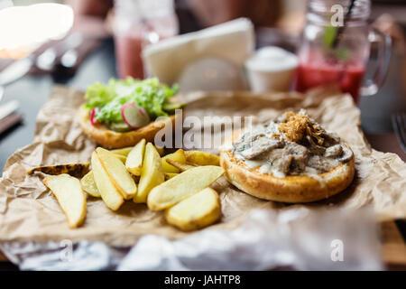 Burger avec des morceaux de boeuf, oignons frits, pommes de terre et légumes. Banque D'Images