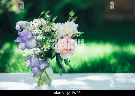 Bouquet de pivoines blanches, camomille et iris fleurs dans vase en verre. Arrière-plan de l'été. Photo teinté Banque D'Images