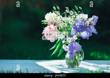 Bouquet de pivoines blanches, camomille et iris fleurs dans vase en verre. Arrière-plan de l'été. Photo teinté Banque D'Images