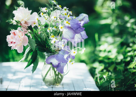 Bouquet de pivoines blanches, camomille et iris fleurs dans vase en verre. Arrière-plan de l'été. Photo teinté Banque D'Images