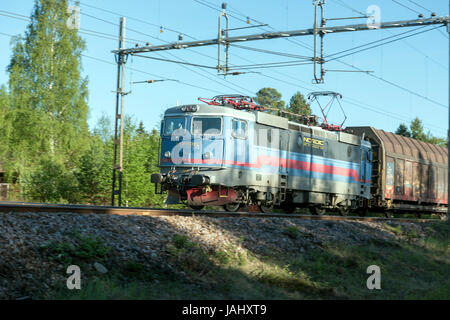 Train de marchandises voyageant à travers la campagne boisée en Suède par une journée ensoleillée, locomotive électrique sur le chemin de fer principal Banque D'Images