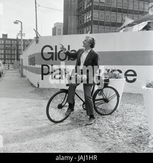 L'acteur et réalisateur Sam Wanamaker sur sa bicyclette à l'extérieur de son site proposé pour le Globe Playhouse Theatre à Londres en 1972. La Sam Wanamaker Playhouse est un théâtre intérieur faisant partie de Shakespeare's Globe, de même que le Globe Theatre, London Bankside sur. Construit en utilisant des plans du 17e siècle pour un théâtre intérieur, la Playhouse rappelle la mise en page et le style du théâtre de Blackfriars, bien qu'il n'est pas une reconstruction exacte. Sa coquille a été construit lors de la construction de la complexité du Globe de Shakespeare, remarquable pour la reconstruction de l'open-air Globe Theatre de la même période. Banque D'Images