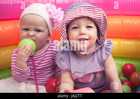 Deux joyeux sourire mignon bébé filles jouant ensemble dans le parc de divertissement avec des jouets symbolisant l'amitié les enfants et enfance heureuse Banque D'Images