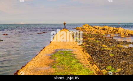 Un pêcheur solitaire se trouve au bout d'une longue promenade au bord de l'eau au point de Peveril Swanage Dorset,, Banque D'Images