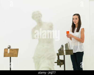 Young caucasian woman standing en face d'une œuvre d'art, tenant un verre de vin dans sa main, parlant, dans un musée d'art Banque D'Images