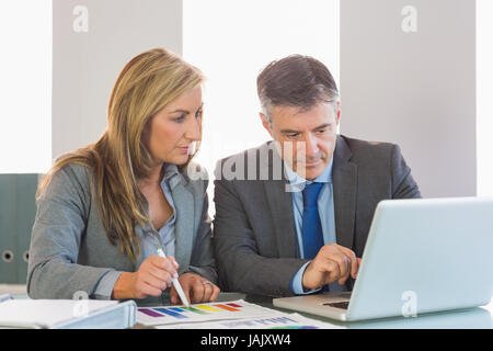 Attentifs mature businessman montrant quelque chose sur ordinateur pour une écoute attentive blond businesswoman at office Banque D'Images