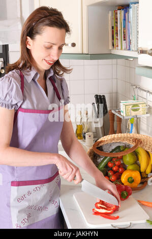 Erwachsene Hausfrau steht in ihrer hellen Einbauküche und bereitet frissen vágott kalódás gyertyán Gemüse zum kochen vor. Banque D'Images