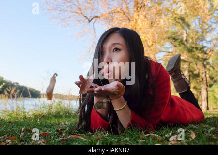 Femme portant sur l'herbe souffle loin une poignée de feuilles Banque D'Images