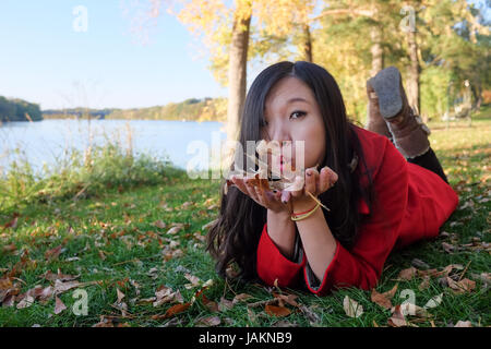 Femme portant sur l'herbe souffle loin une poignée de feuilles Banque D'Images