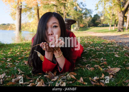 Femme portant sur l'herbe souffle loin une poignée de feuilles Banque D'Images