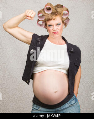 Young pregnant woman in curlers fléchissant ses biceps Banque D'Images