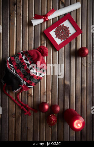 Image de flocon rouge dans l'image, des boules de jouet, cap, bougie allumée et enveloppé dans du papier avec ruban de soie rouge sur fond de bois Banque D'Images