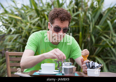 Mid adult man drinking tasse de café ou de thé à l'extérieur en plein air holding glace au chocolat dans la main Banque D'Images