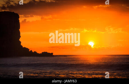 Lever de soleil rouge orange brillant à travers les nuages au-dessus de l'horizon de l'océan Pacifique au large de la plage d'Avalon à Sydney plages du Nord. Surface de l'océan reflète la lumière du soleil. Banque D'Images