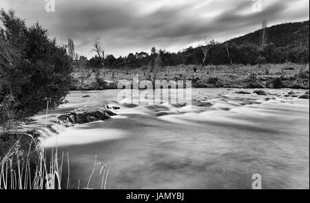 Noir blanc de Thredbo floue des radiers sur la rivière au coucher du soleil entre collines et montagnes dans le parc national de Kosciuszko. Banque D'Images