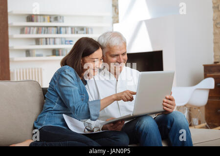 Couple à l'aide de leur ordinateur portable pour payer leurs factures à la maison dans le salon Banque D'Images